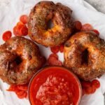 Three pizza protein bagels on parchment paper served with marinara sauce and pepperoni