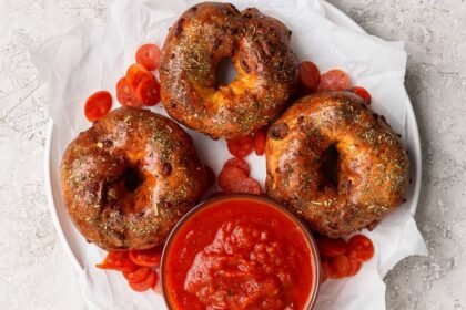 Three pizza protein bagels on parchment paper served with marinara sauce and pepperoni