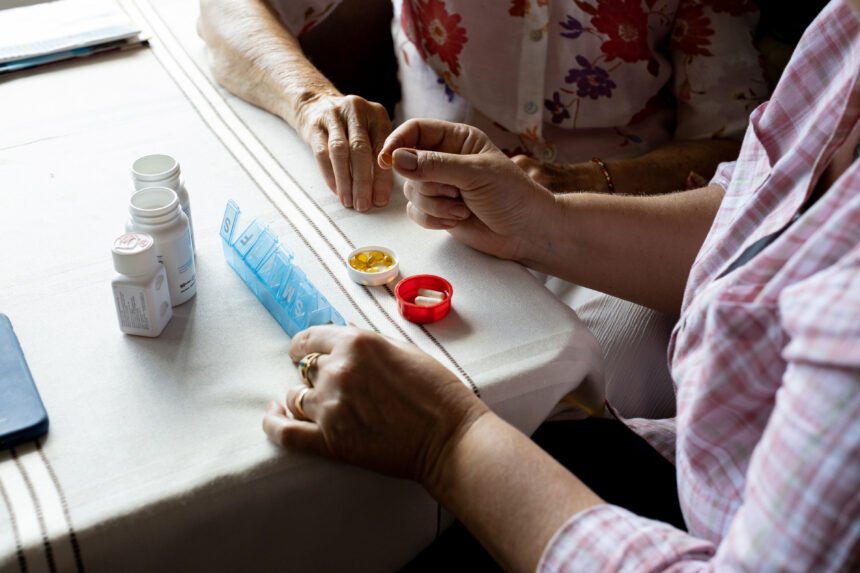 A close up shot of a woman sorting daily medication for a senior woman seated beside her.