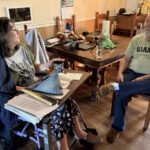 A husband sits in a chair conversing with his wife, who is in a wheelchair.