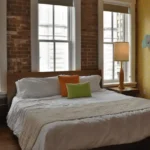 Stylish guest room at The Dwell Hotel in Chattanooga, TN featuring exposed brick, modern lamps, retro wallpaper, and a cozy king bed with colorful accent pillows. Review