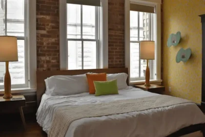 Stylish guest room at The Dwell Hotel in Chattanooga, TN featuring exposed brick, modern lamps, retro wallpaper, and a cozy king bed with colorful accent pillows. Review