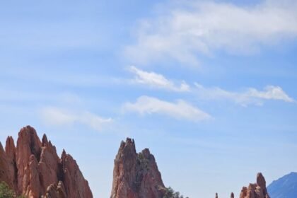 Towering red sandstone spires and cliffs surrounded by evergreens at Garden of the Gods, with dramatic peaks and blue sky.