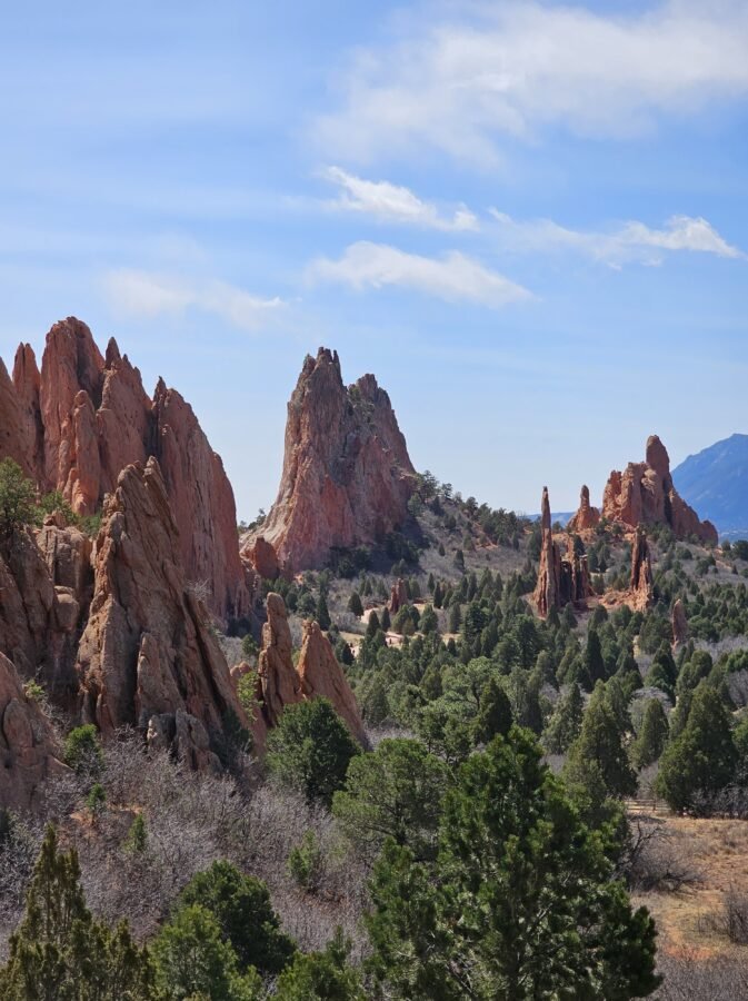 Towering red sandstone spires and cliffs surrounded by evergreens at Garden of the Gods, with dramatic peaks and blue sky.