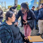A street medicine nurse holds the end of a stethoscope to a woman's chest.