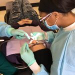 A photo from above of a person lying in a dental chair having work done. A dentist and assistant sit on either side of the patient's head.