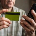 A senior man looks at a credit card while on his phone