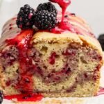 A loaf of blackberry bread topped with blackberries and a drizzle of blackberry sauce.
