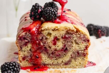 A loaf of blackberry bread topped with blackberries and a drizzle of blackberry sauce.