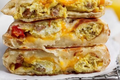 Three breakfast stuffed flatbreads stacked, filled with scrambled eggs, sausage, melted cheese, and some visible tomato pieces.