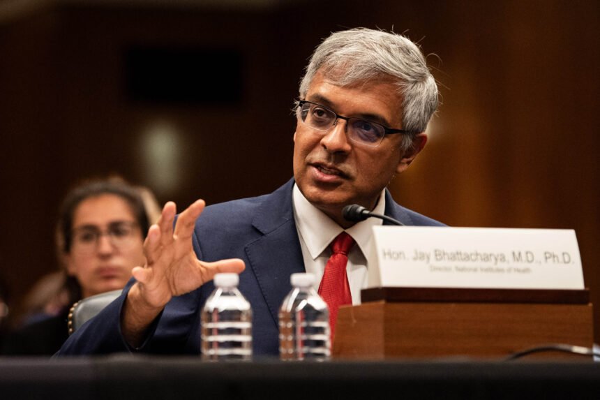 Jay Bhattacharya speaks while sitting at a table with his nameplate, and two water bottles, in front of him.