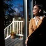 A woman in a yellow cardigan sits in front of a window, staring out