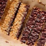 Rectangular chocolate and peanut butter crispy bars with a sprinkle of sea salt, arranged on parchment paper.