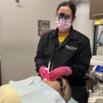 A dental hygienist works on a patient in a dental chair.