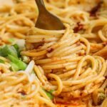A fork twirls spaghetti coated in a creamy, orange-hued sauce with green onions sprinkled on top.