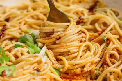 A fork twirls spaghetti coated in a creamy, orange-hued sauce with green onions sprinkled on top.
