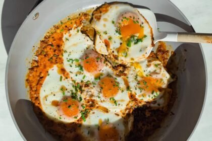 Fried eggs cooked in a skillet with tomato sauce and herbs, with a spatula lifting one egg.