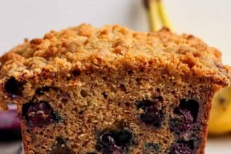 Close-up of a sliced loaf of blueberry banana bread with a crumbly topping, showing visible blueberries inside the moist bread.