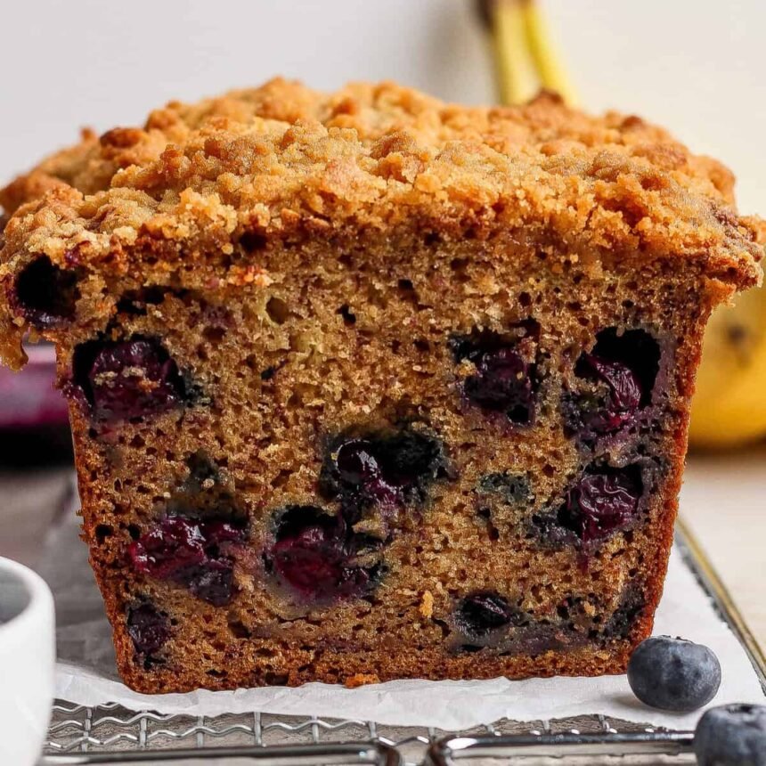 Close-up of a sliced loaf of blueberry banana bread with a crumbly topping, showing visible blueberries inside the moist bread.