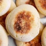 A close-up photo of several golden-brown English muffins sprinkled with cornmeal.