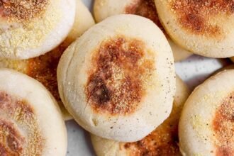 A close-up photo of several golden-brown English muffins sprinkled with cornmeal.