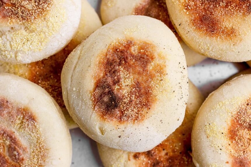 A close-up photo of several golden-brown English muffins sprinkled with cornmeal.