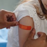 A doctor applies a bandage to a young girl's arm after she receives a vaccine.