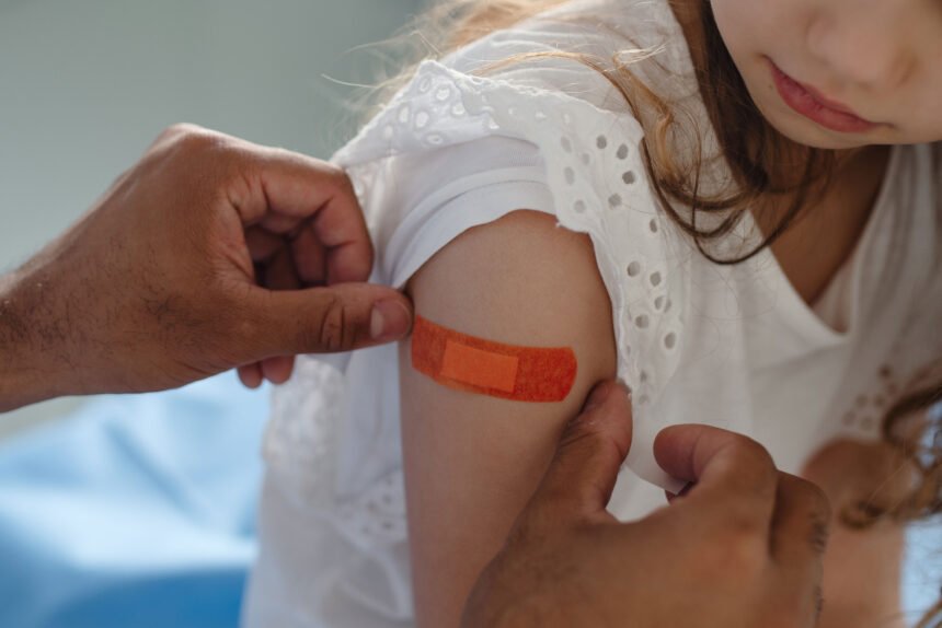 A doctor applies a bandage to a young girl's arm after she receives a vaccine.