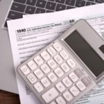 A set of tax forms and a calculator rest on top of a laptop.