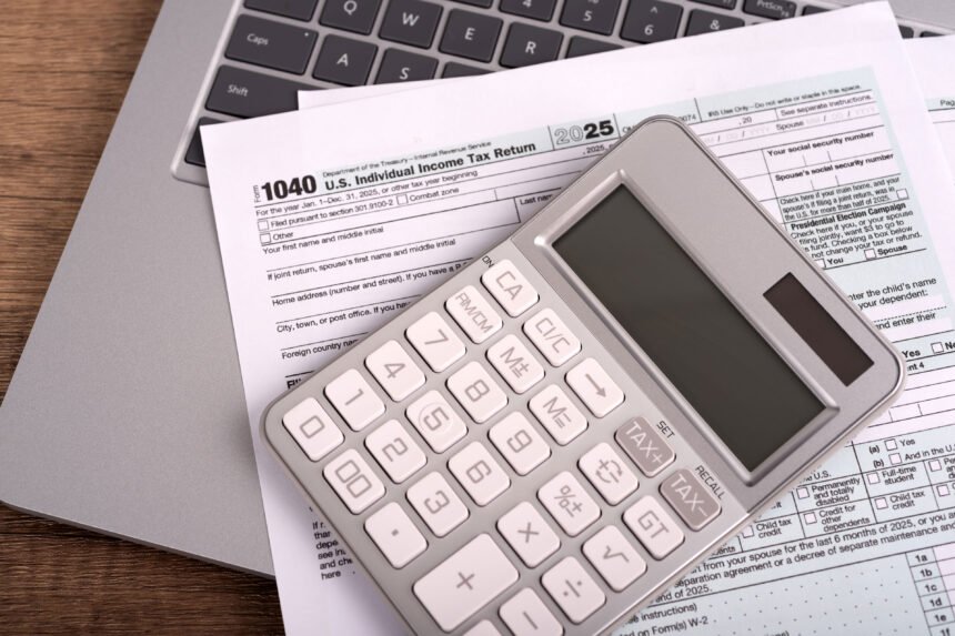 A set of tax forms and a calculator rest on top of a laptop.