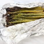 grilled asparagus in foil on a white plate with lemon wedges