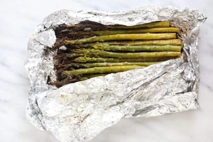 grilled asparagus in foil on a white plate with lemon wedges