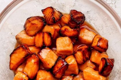 Cubes of cooked salmon in a glass bowl, coated with a shiny, dark caramelized glaze.
