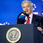A man with white hair stands behind a lectern with the seal of the President of the United States on it, and speaks into a microphone.