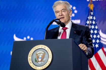 A man with white hair stands behind a lectern with the seal of the President of the United States on it, and speaks into a microphone.