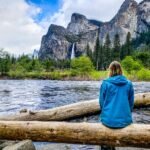 woman sitting on log looking at view of Bridalveil falls from yosemite valley