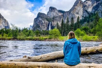 woman sitting on log looking at view of Bridalveil falls from yosemite valley