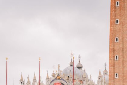 A varnished wooden water taxi and cargo boats on a Venice canal in front of the ornate white marble facade of the Scuola Grande di San Marco