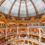 The stained glass and gilded dome of Galeries Lafayette Haussmann seen from the ground floor, with shoppers along the tiers of balconies below it