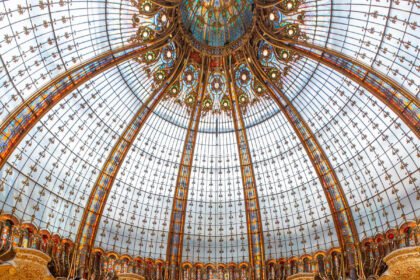 The stained glass and gilded dome of Galeries Lafayette Haussmann seen from the ground floor, with shoppers along the tiers of balconies below it