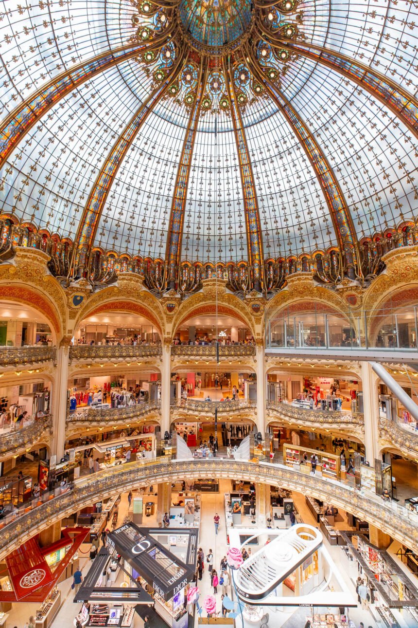 The stained glass and gilded dome of Galeries Lafayette Haussmann seen from the ground floor, with shoppers along the tiers of balconies below it