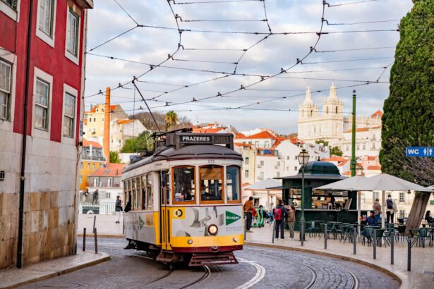 A yellow vintage Lisbon tram rounding a curve on cobblestone tracks with pastel buildings and the domed church of Sao Vicente de Fora rising in the background