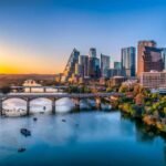 Austin, Texas- Cityscape with Colorado River in the middle against the sunset sky. There are boats near under the bridge at the front and a view of skycrapers on the side with reflective glass walls.